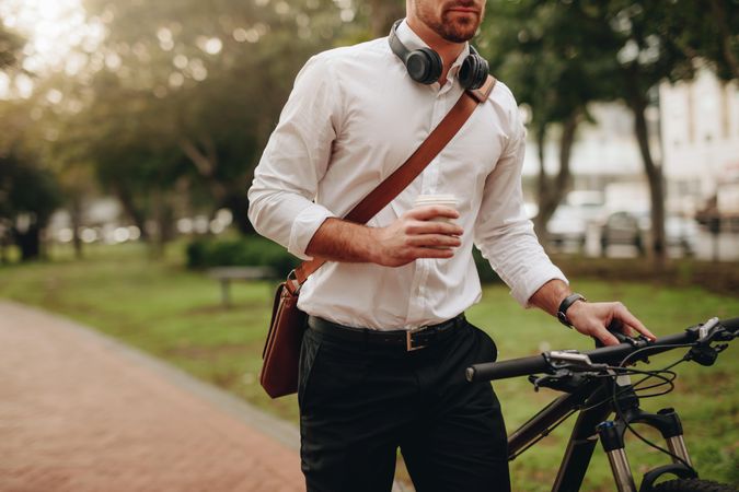 Businessman holding a coffee cup and walking to office taking his bicycle along