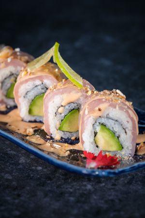 Yummy sushi rolls decorated with avocado served on tray