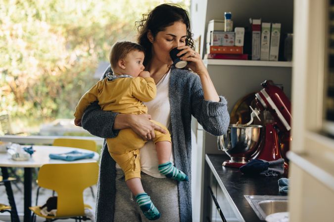 Mother carrying her infant having a cup of coffee in the morning