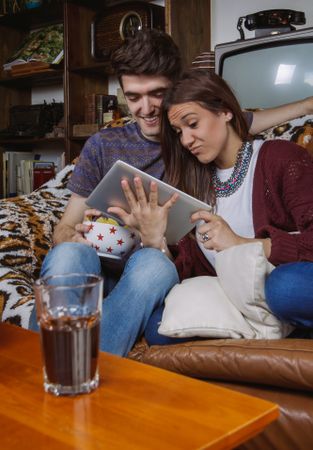 Young couple laughing and looking tablet sitting on sofa