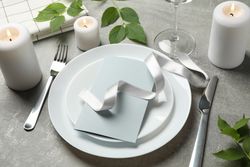 Composition of table setting with candles, leaves and cutlery on gray background