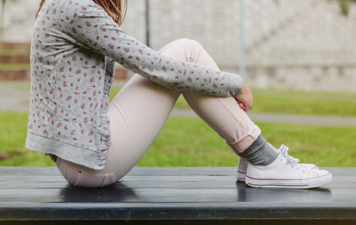 Woman wearing cardigan and pink jeans sitting on park bench