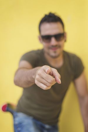 Male pointing at camera in front of yellow wall outside, vertical