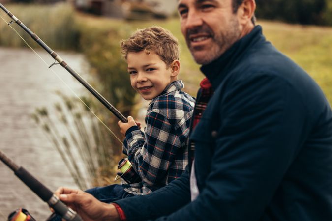 Young child holding fishing rod with father and looking at camera