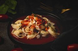 Plate of delicious ravioli with tomato sauce served on table