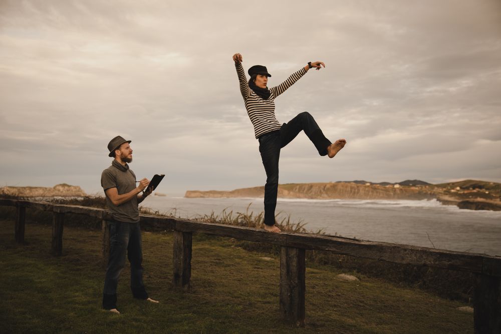 Couple holding hands and jumping on bench on shore near water