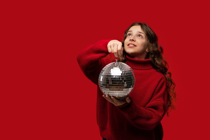 Smiling girl in red sweater holds disco ball, looking up