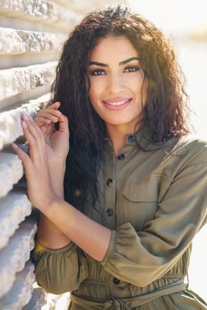 Middle Eastern woman smiling while resting on outside wall