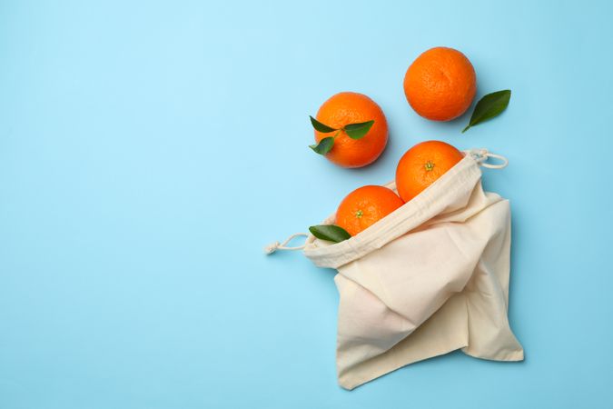 Cotton bag with ripe mandarins on blue background