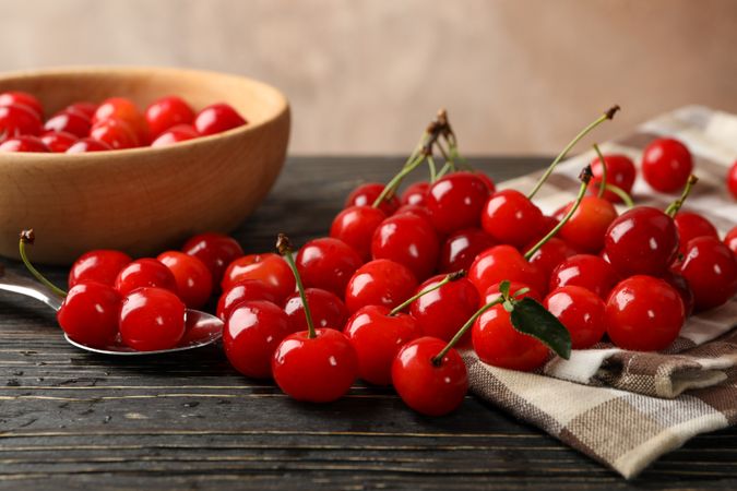 Towel, spoon and bowl with cherry on wooden background, close up