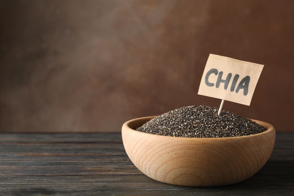 Wooden bowl and word Chia on wood background, copy space