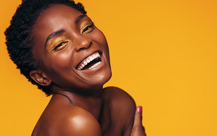 Close up of young woman with makeup laughing against yellow background
