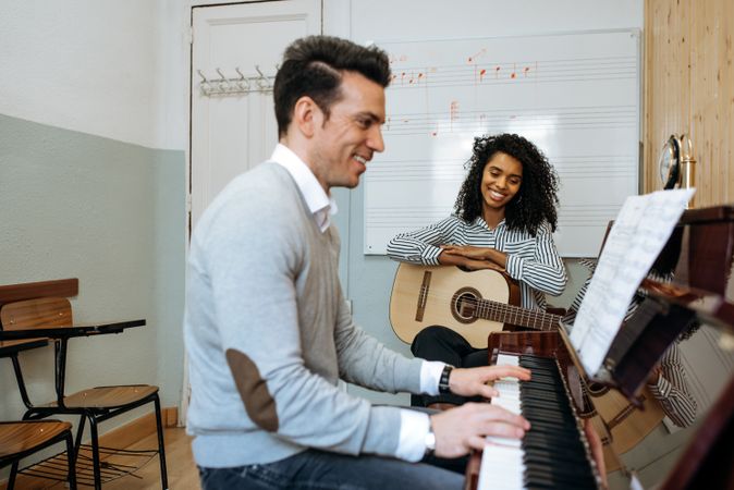 Man playing piano near woman playing guitar in studio