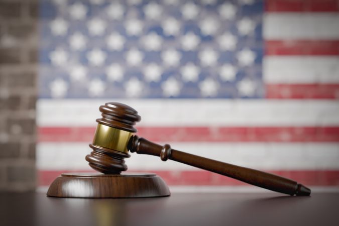American Flag On Wall Behind Gavel Resting on Table.