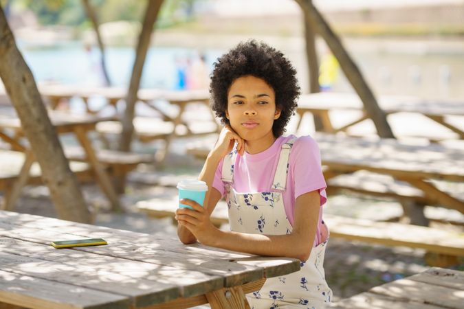 Woman sitting on park table with to go cup looking in the distance