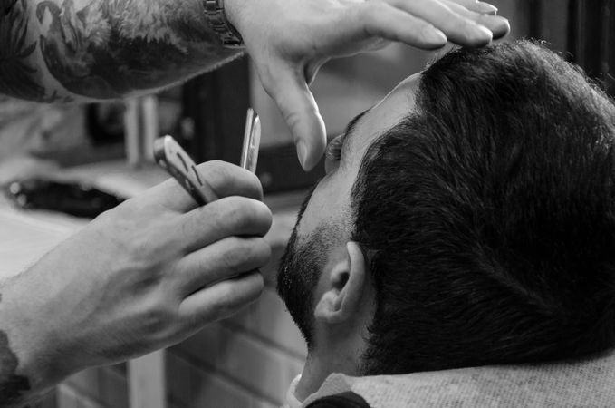 Monochrome photo of man at the barber getting his beard done