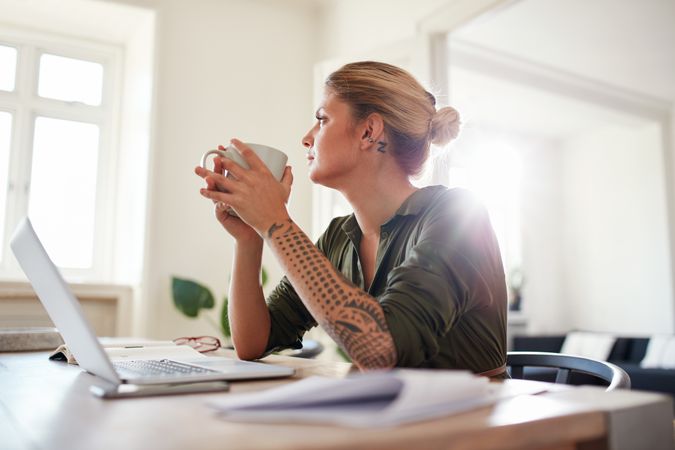 Indoor shot of young woman with coffee looking away and thinking