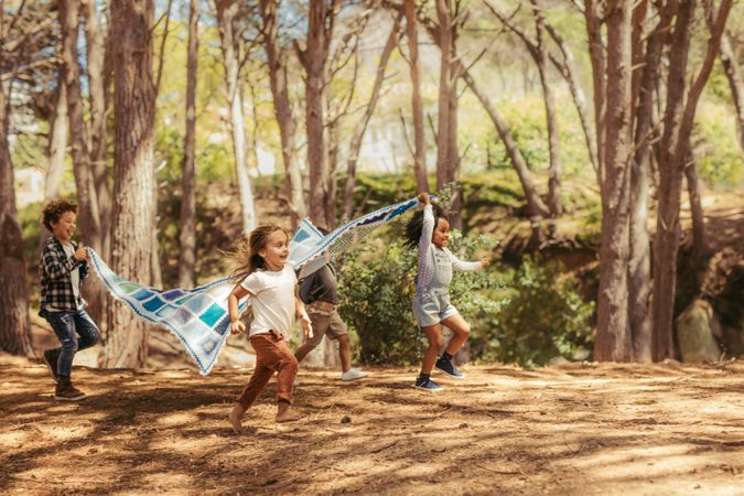 Four kids running in park with picnic blanket