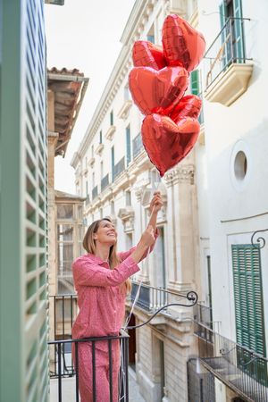 Woman with bunch of red heart foil balloons on balcony