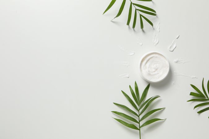 Jar with cream and twigs on light background, space for text