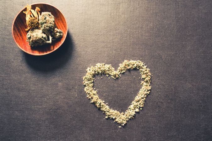 Dried marijuana in the shape of a heart and wooden container of bud