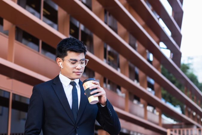 Handsome Asian businessman with takeaway coffee in city