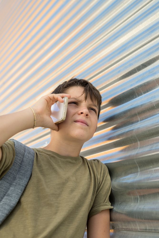 Boy talking on smartphone leaning on metal wall