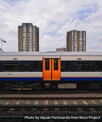 Centered shot of subway car with orange doors outside with buildings in background in London 5r9p10