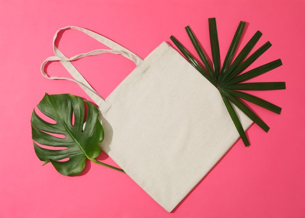 Eco bag and palm leaves on color background, top view