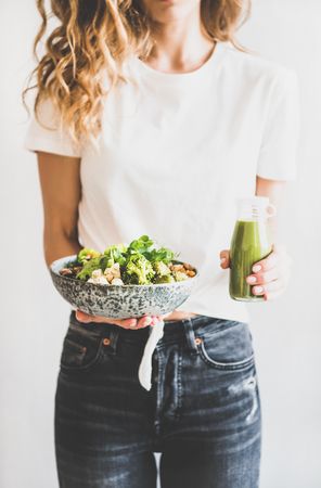 Woman in jeans standing holding vegetarian bowl and green smoothie