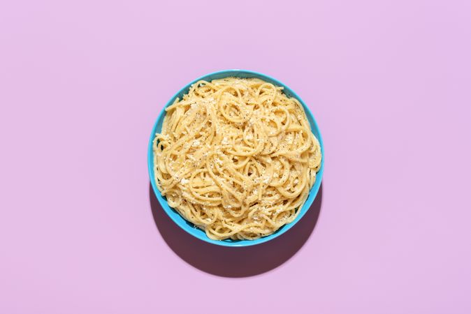 Spaghetti with cheese and black pepper, top view on a purple background