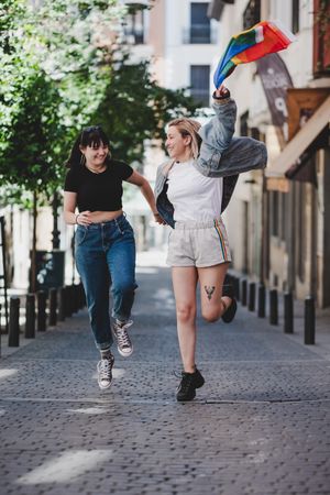 Lesbian couple with LGBT flag walking on street