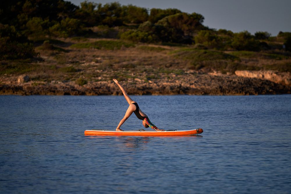 Sportswoman taking Downward Facing Dog pose on paddleboard in se