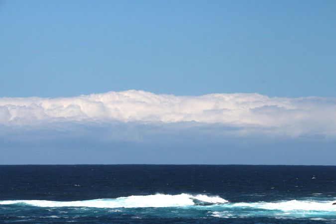 Ocean waves rolling gently under a bright blue sky with clouds in the distance