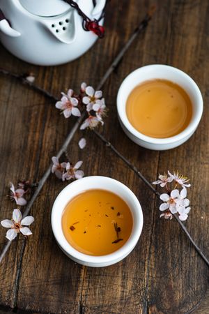 Top view of cups of green tea with floral petals on wooden board