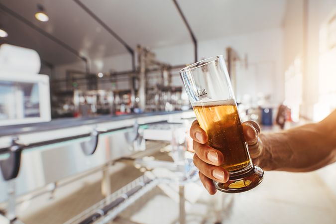 Cropped shot of male holding beer glass in warehouse