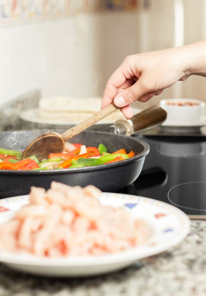 Closeup of female cooking vegetables and chicken in a pan