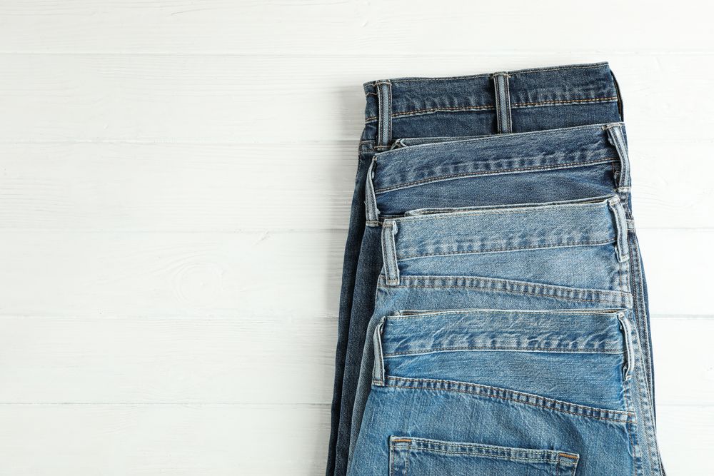 Different jeans folded on a wooden background, space for text