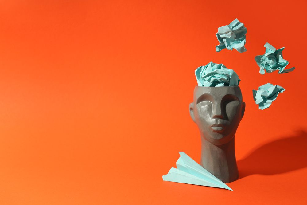 Grey bust of head on red background with crumpled paper, copy space