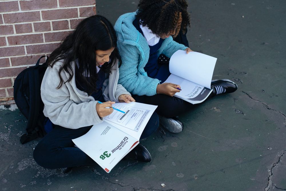 Boy and girl with school bags sitting on ground in school yard