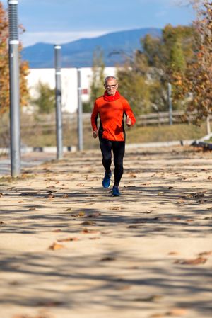 Older man in leggings and windbreaker jogging in park