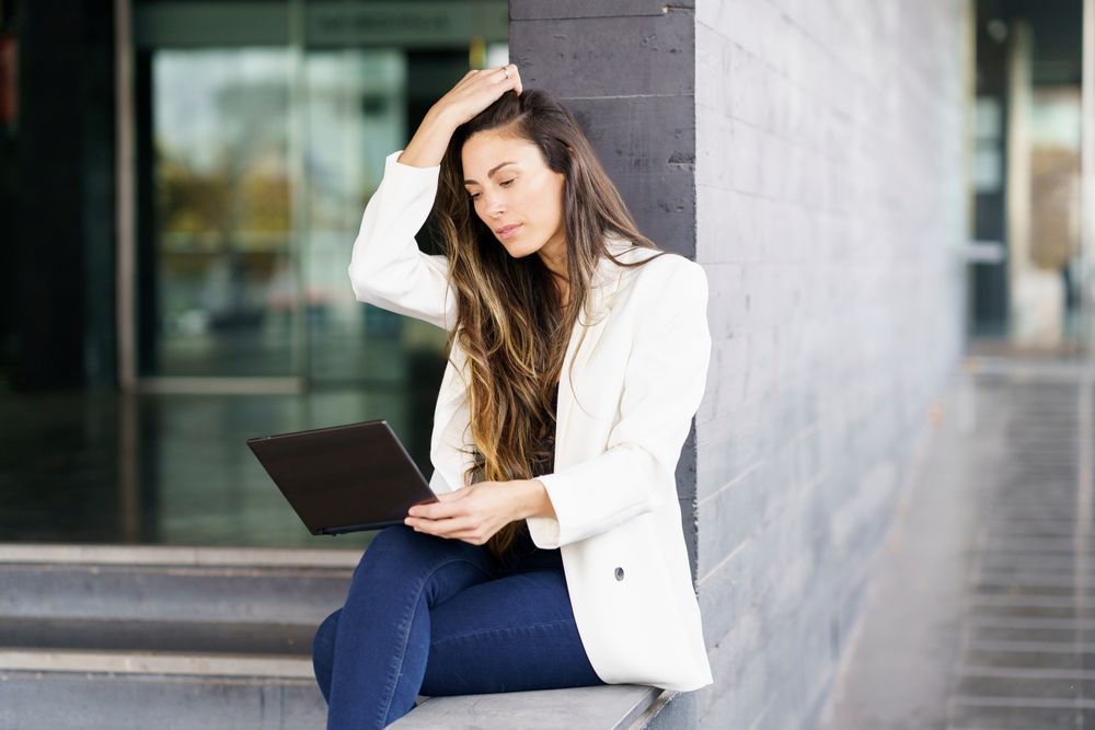 A woman in a stylish blazer is engaged with her tablet in a modern urban setting