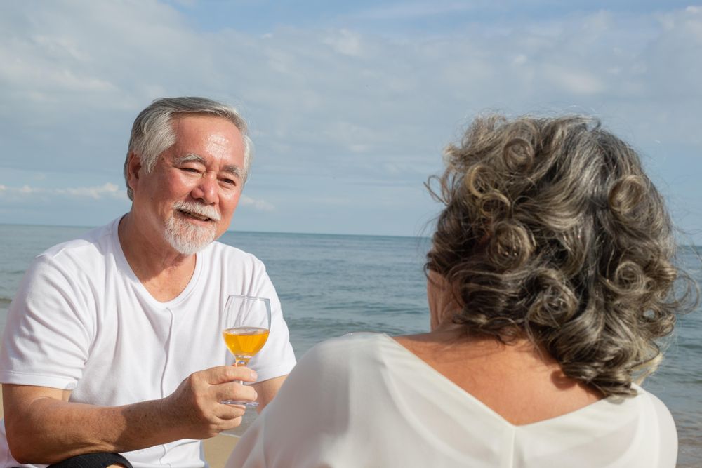 Smiling Asian couple relaxing at the waterfront with wine