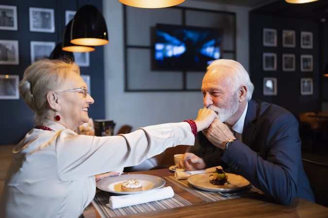 Older man kissing hand of smiling woman at restaurant date