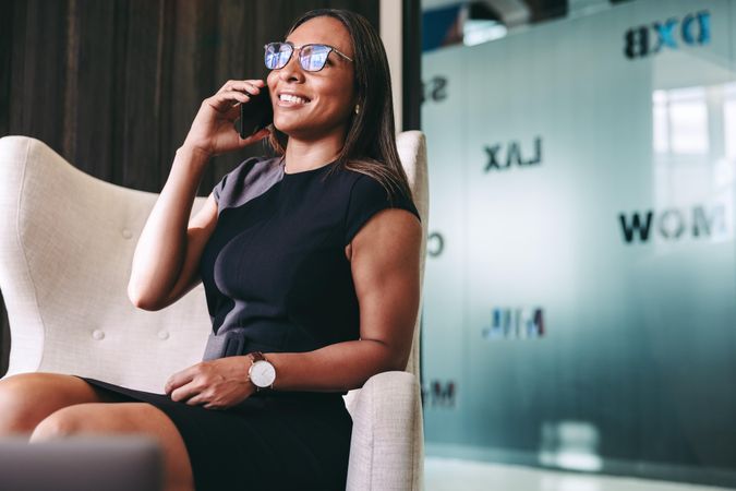 Happy young businesswoman smiling while speaking on her cellphone in a modern office