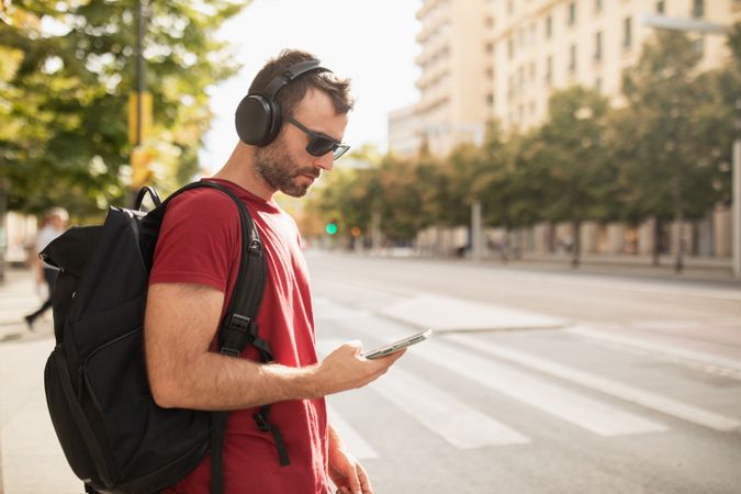 A young man wearing sunglasses, listening to music and looking at his smartphone while visiting a city in Spain