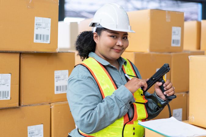 Woman in safety gear working in distribution center checking bar codes on stock