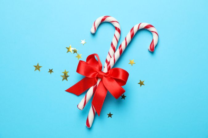 Sweet candy canes and bow on color background, space for text