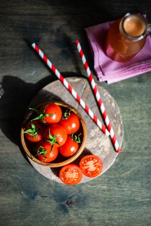 Top view of bowl of fresh tomatoes with striped straws and carafe of juice