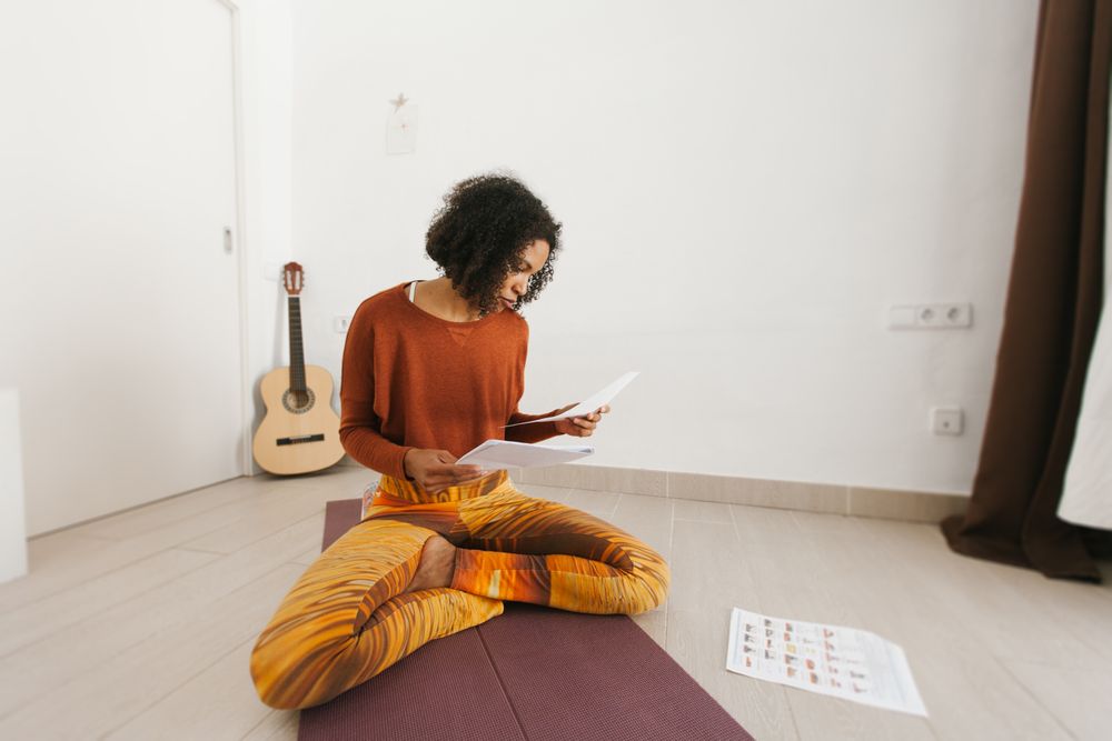 Sportive woman sitting with legs crossed on floor studying routine paper
